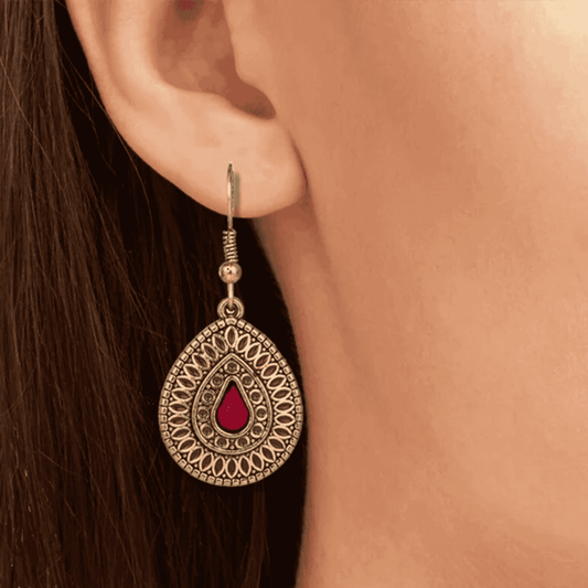 Close-up of a single antique silver teardrop drop earring with red enamel worn on an ear.