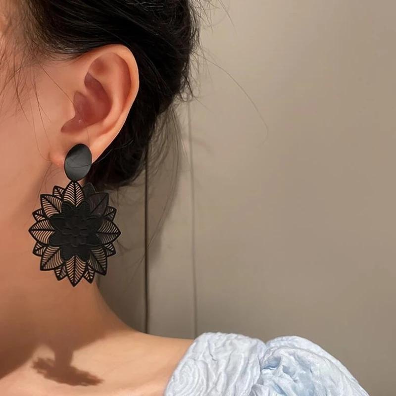 A pair of black geometric flower drop earrings with a matte finish, resting on a white surface.