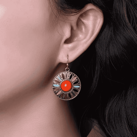 A woman wearing a single round boho earring with a central red stone and light blue and black enamel details, showcasing its size and fit.
