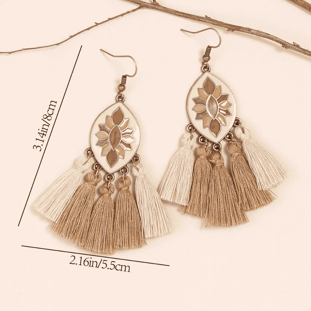 A pair of boho earrings with cream enamel, brown floral design, and layered beige and brown tassels, with size measurements of 3.14in/8cm length and 2.16in/5.5cm width.