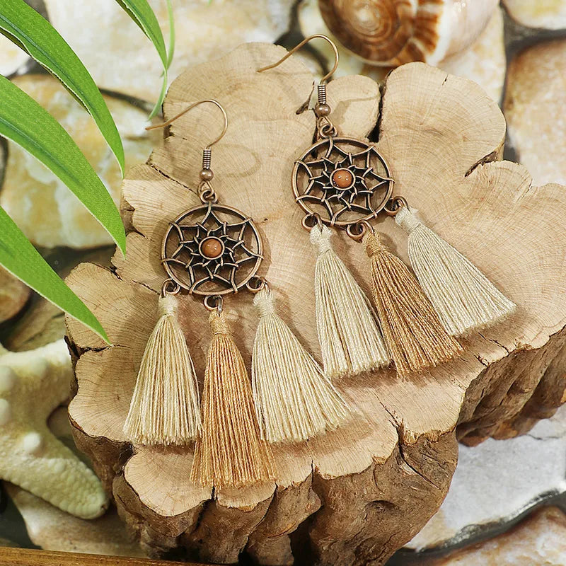 Pair of boho oxidised dreamcatcher tassel earrings with earthy-toned tassels displayed on a wooden block.