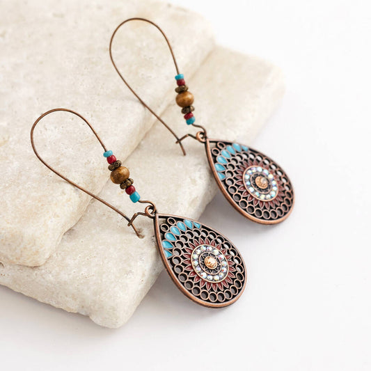 A pair of boho earrings with oxidised metal teardrop pendants and colorful beads, displayed on white textured rocks.