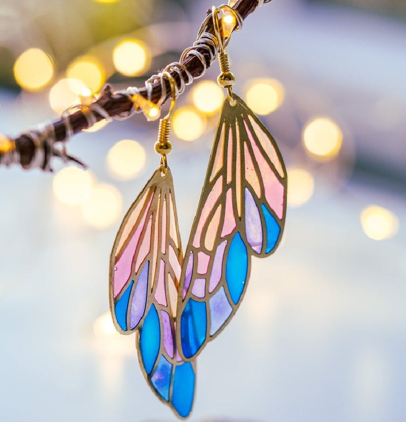 A close-up of a pair of gold-tone butterfly wing boho earrings with vibrant blue, purple, and pink resin, highlighting the intricate details and colors.