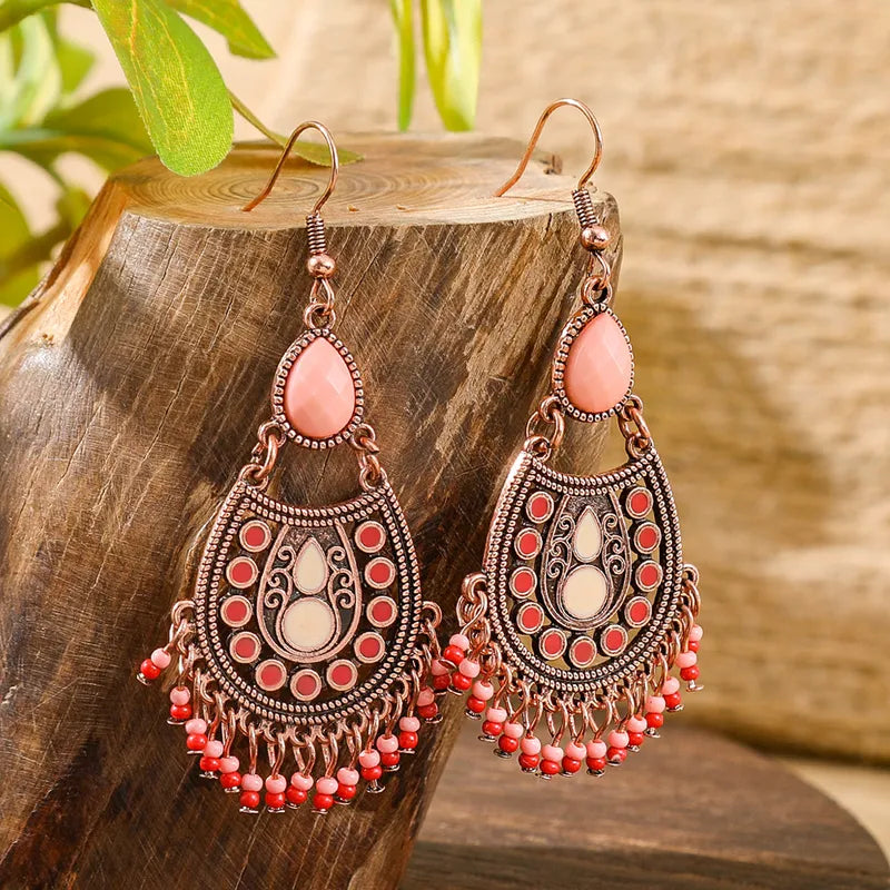 Pair of oxidised earrings with pink teardrop stones, red and cream enamel accents, and dangling pink and red beads, displayed on a wooden block.