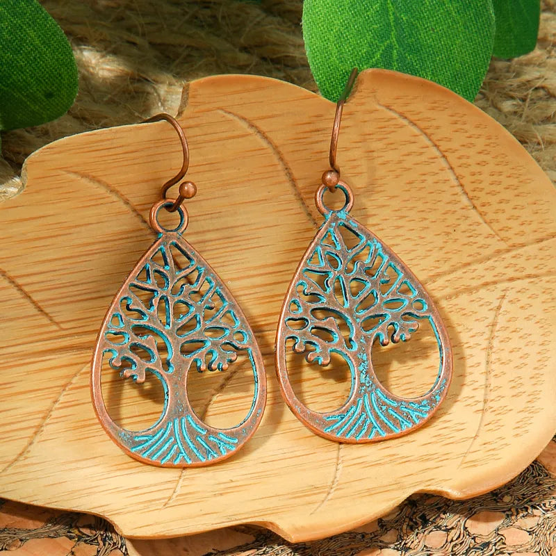 Pair of oxidised earrings, teardrop shape with a Tree of Life design and blue accents, displayed on a light brown leaf-shaped wooden tray. These are oxidised earrings.