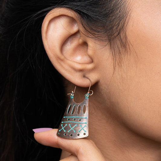 A close-up of a woman wearing a single oxidised earring with a tribal geometric design, held by her hand, showcasing its size and detail.