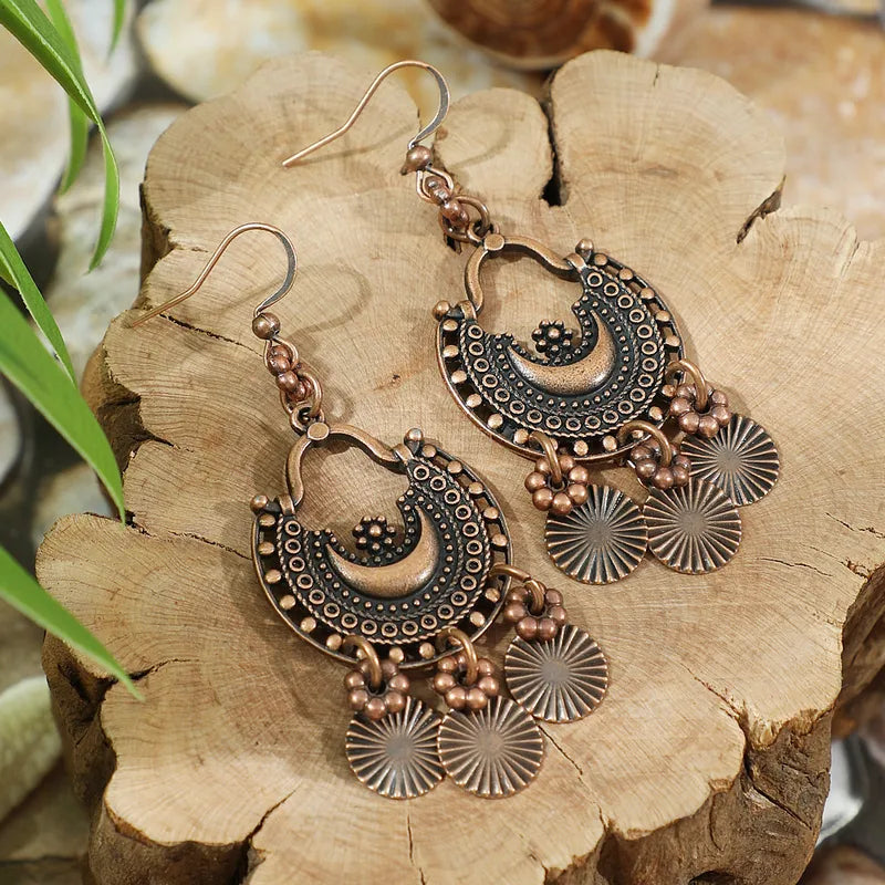 A pair of oxidised earrings with an antique crescent design and dangling circular charms, resting on a rustic wooden surface, showcasing their bohemian appeal.