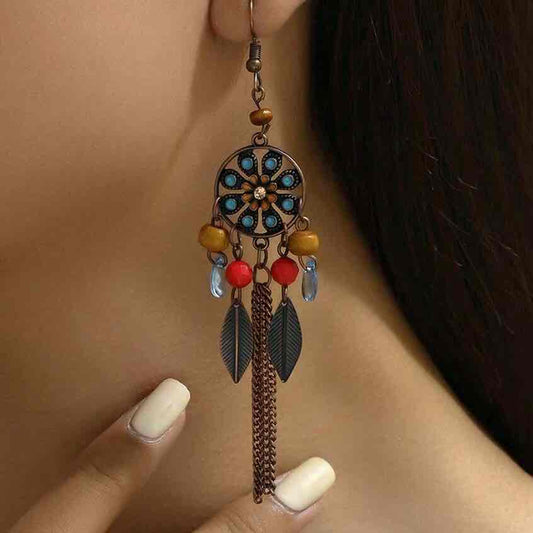 Close-up of a woman wearing a single oxidised dreamcatcher long earring with turquoise and red beads.