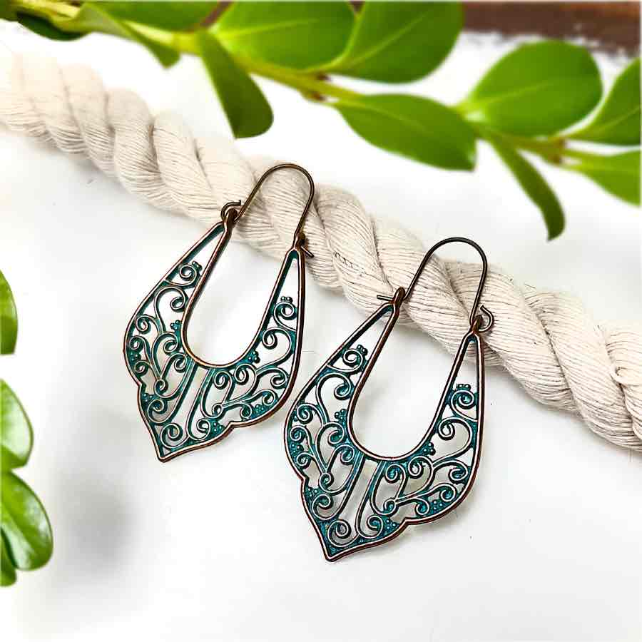 Close-up of two oxidised filigree drop earrings with a patina green finish, showcasing the intricate details on a wooden surface.