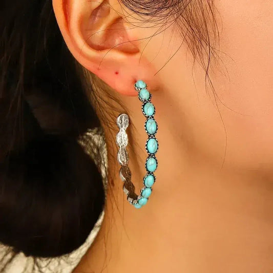 Close-up of the top part of an oxidised silver hoop earring, showing oval turquoise stones and the ear post against a wooden