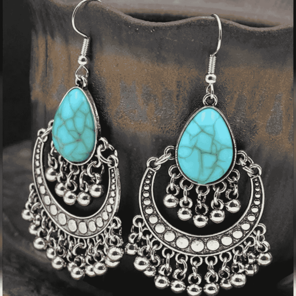 A pair of oxidised silver drop earrings with teardrop turquoise stones, showcased against a light wooden background.