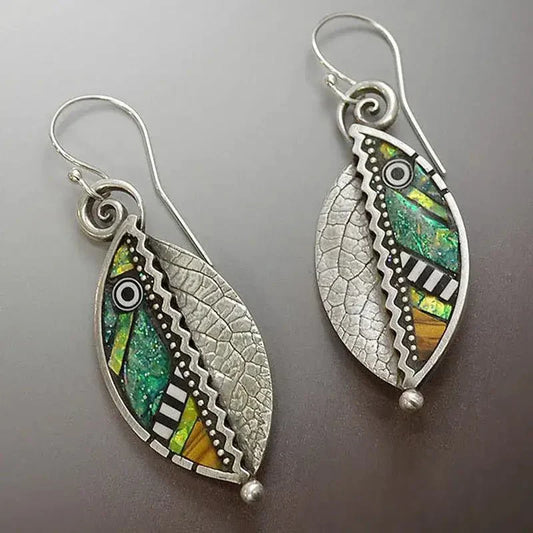 Close-up of oxidised earrings with a leaf shape, showcasing vibrant mosaic patterns in green, yellow, and orange, alongside textured silver filigree.