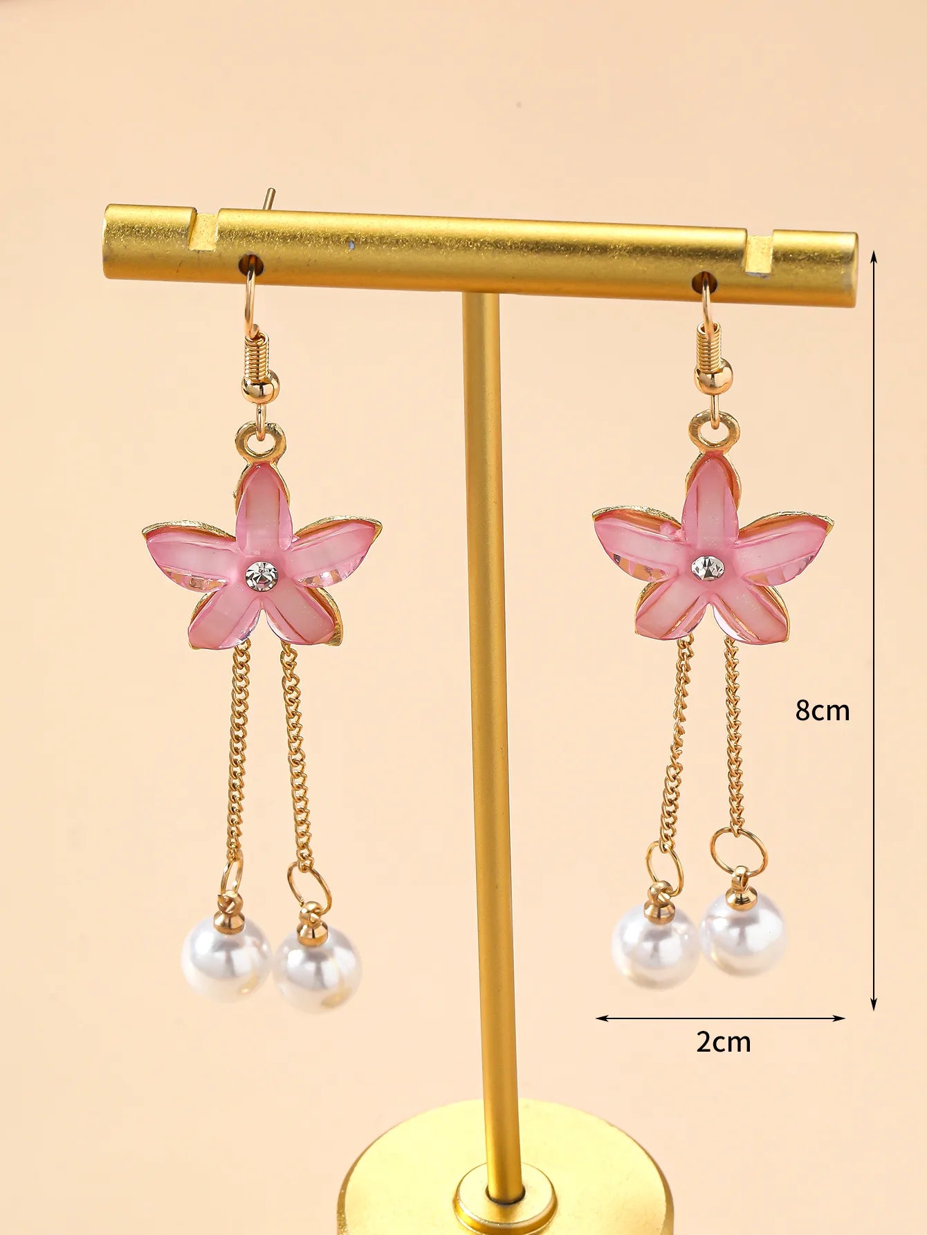 A pair of pink floral drop earrings with pearl chains on a beige surface, viewed from a slightly different angle.