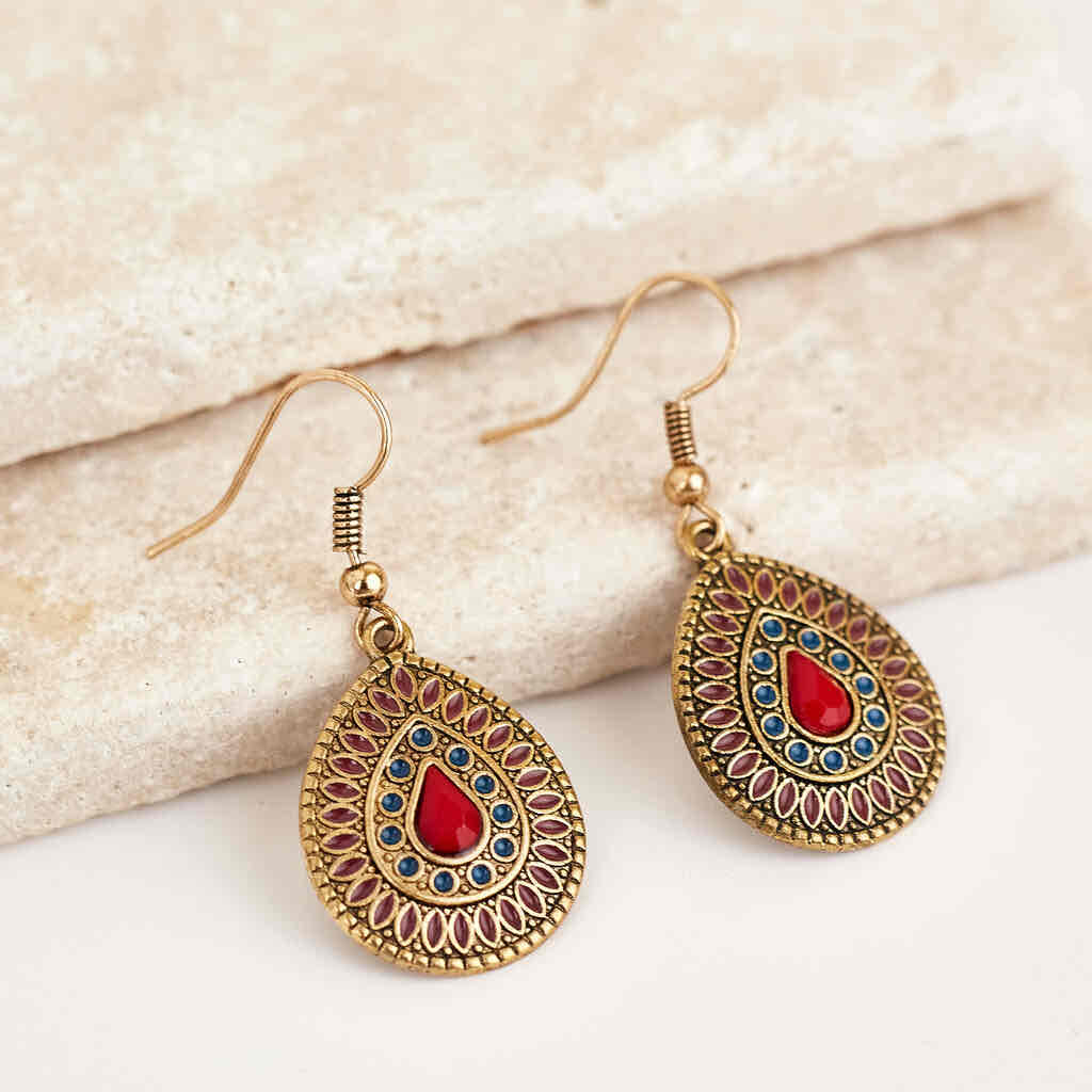 Pair of antique gold teardrop drop earrings with red and blue enamel on a light textured surface.