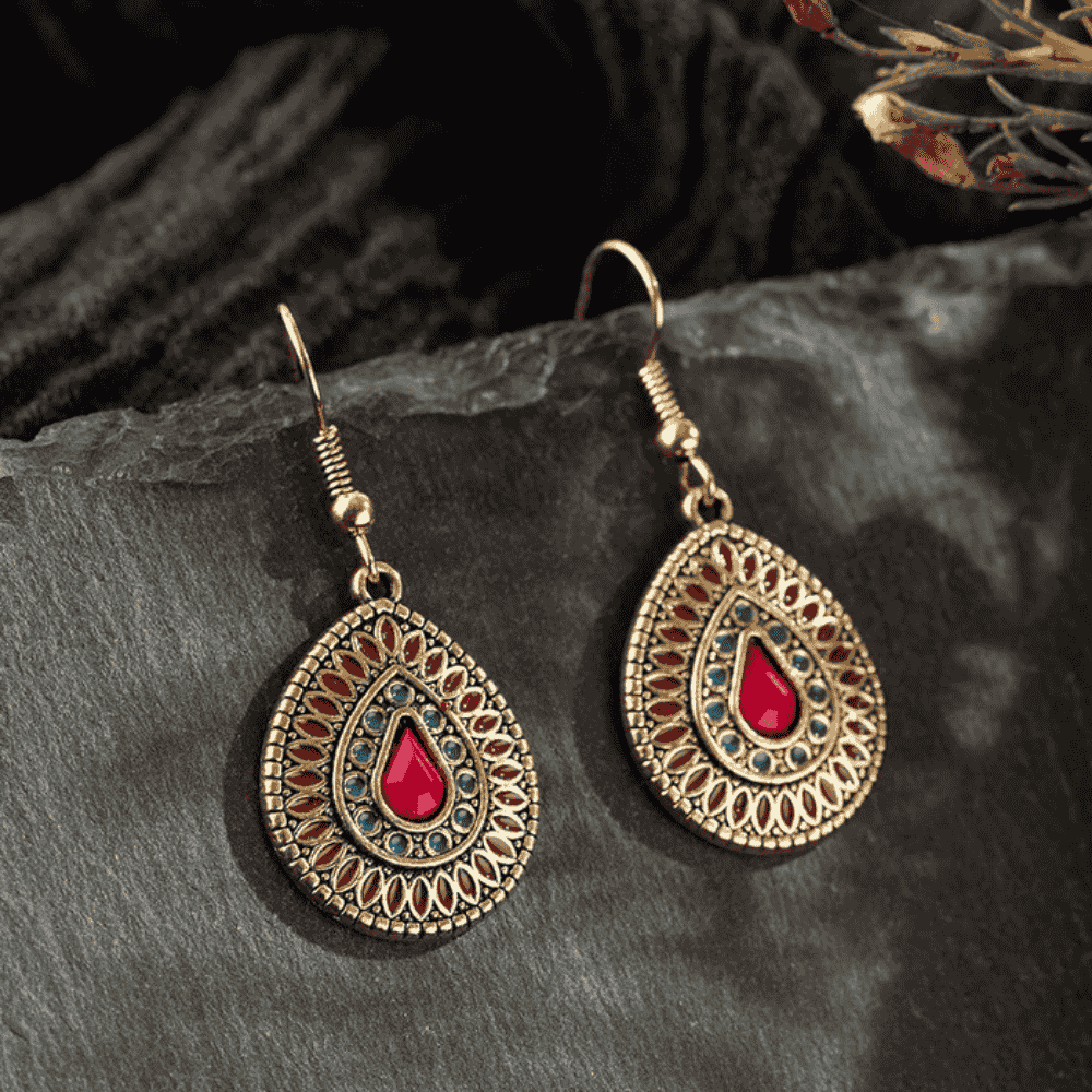 Pair of antique gold teardrop drop earrings with red and blue enamel on a dark textured surface.
