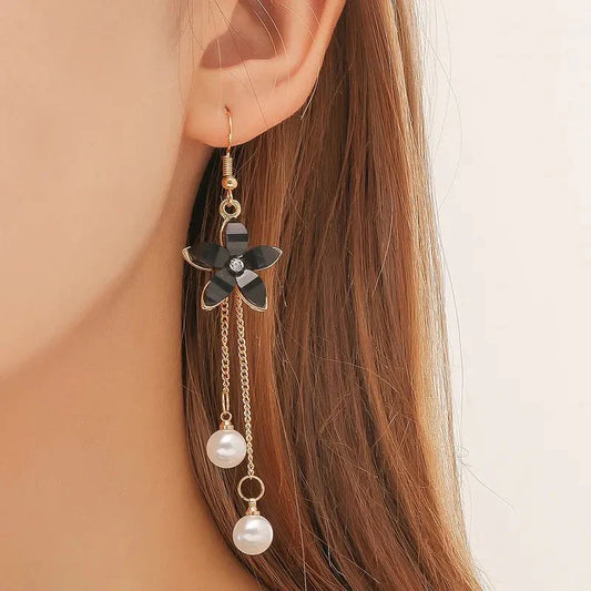 Close-up of a woman wearing a single black floral long earring with pearl chain dangle.