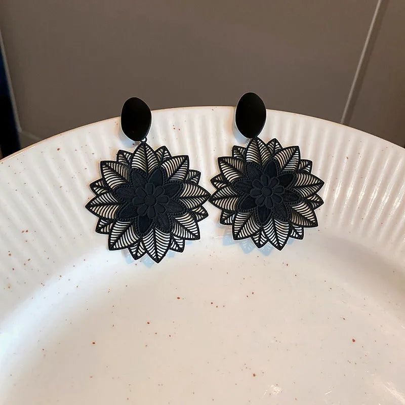 A pair of black geometric flower drop earrings displayed on a white textured plate.
