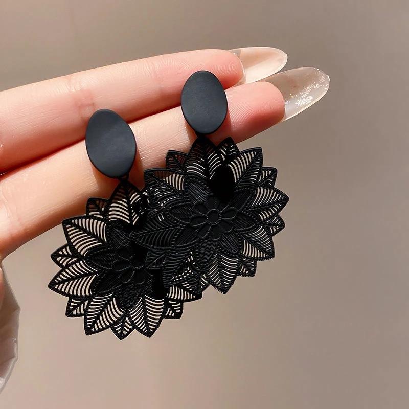 A hand holding a pair of black geometric flower drop earrings, showcasing the intricate design.