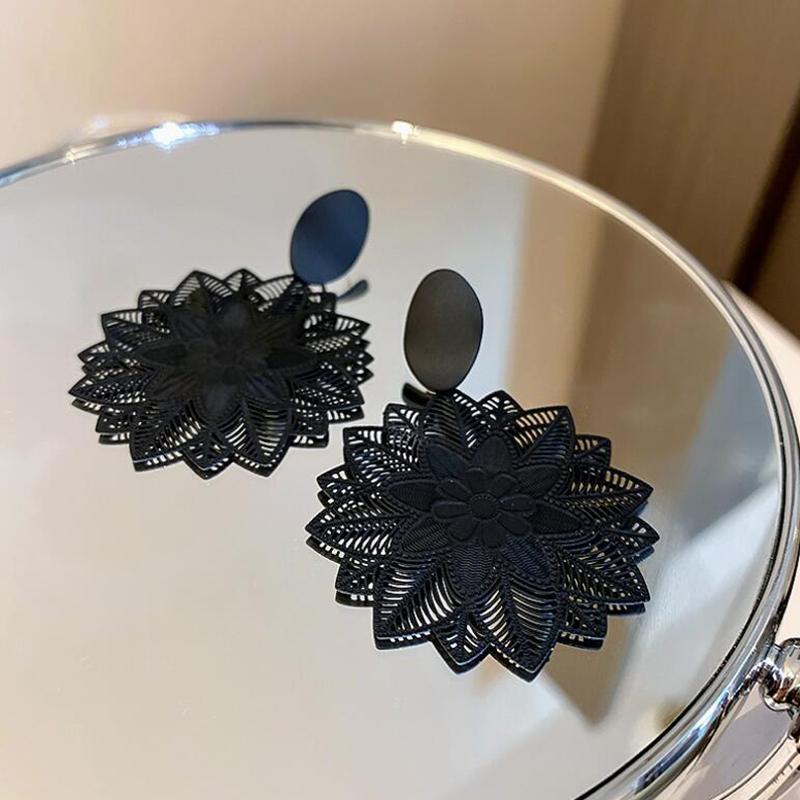 A close-up of a black geometric flower drop earring on a white textured surface.