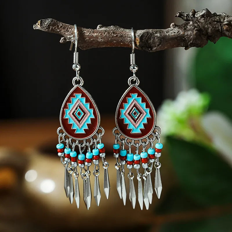 A pair of bohemian alloy teardrop dangle earrings with a geometric pattern in red, blue, and pink, hanging from a tree branch.