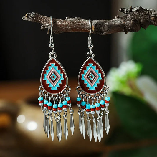 A pair of bohemian alloy teardrop dangle earrings with a geometric pattern in red, blue, and pink, hanging from a tree branch.