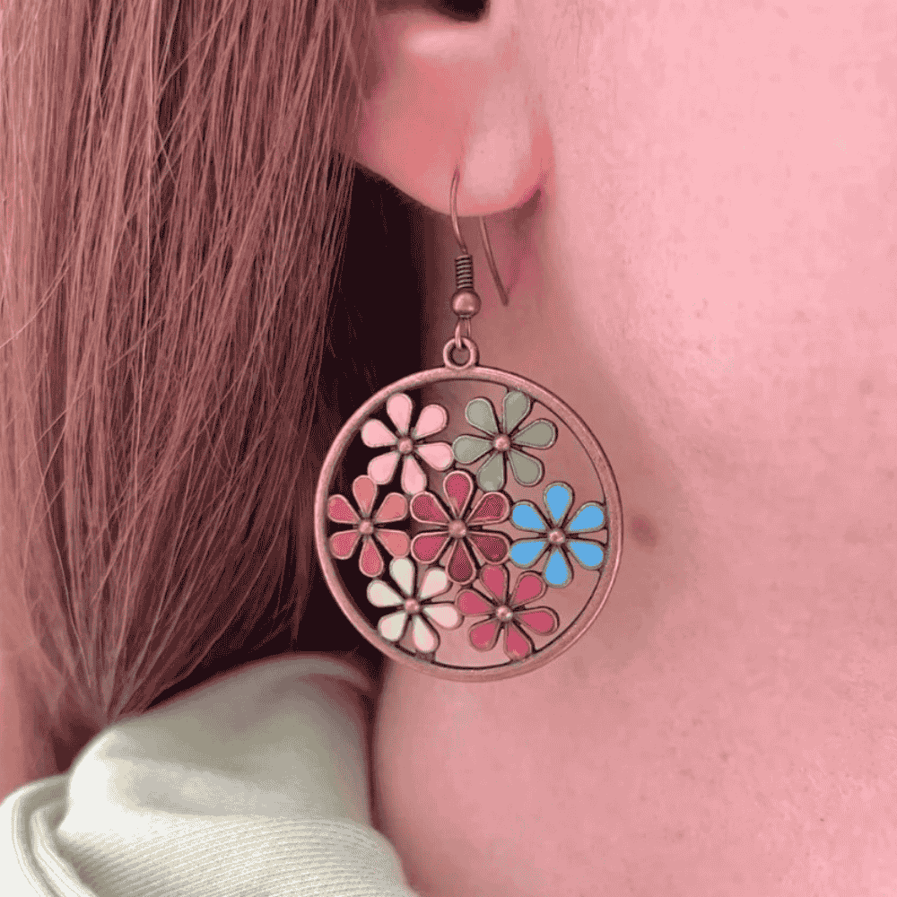 Close-up of a woman wearing a single copper-tone boho earring with multi-colored enamel flowers in a circular frame.