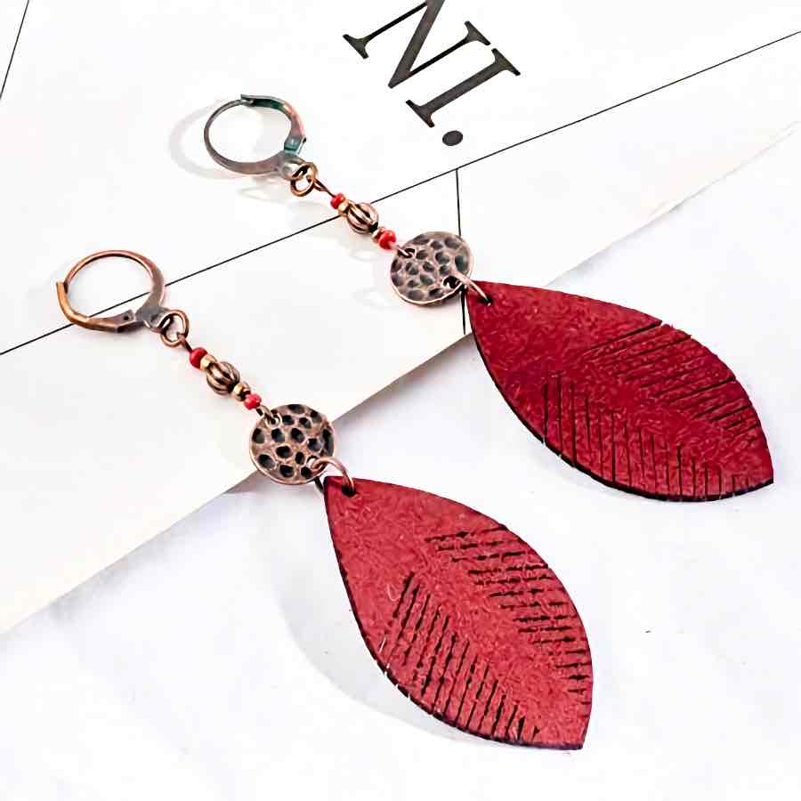A pair of red leaf leather boho earrings with bronze accents and small red beads, displayed on a white surface with a partial 'NI' text.