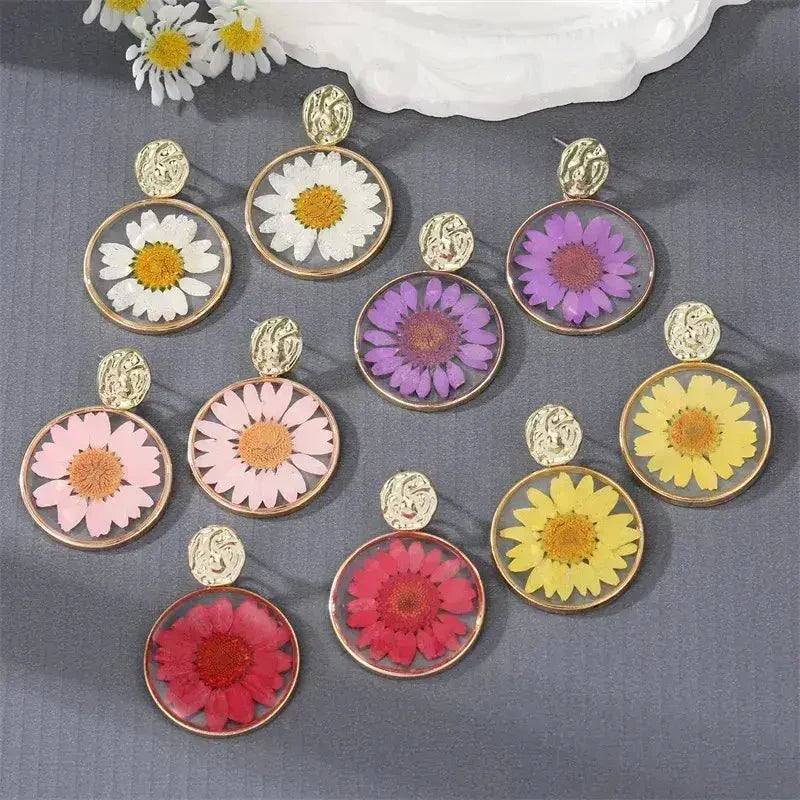 A collection of colorful boho earrings featuring pressed flowers in clear resin, set against a gray background.