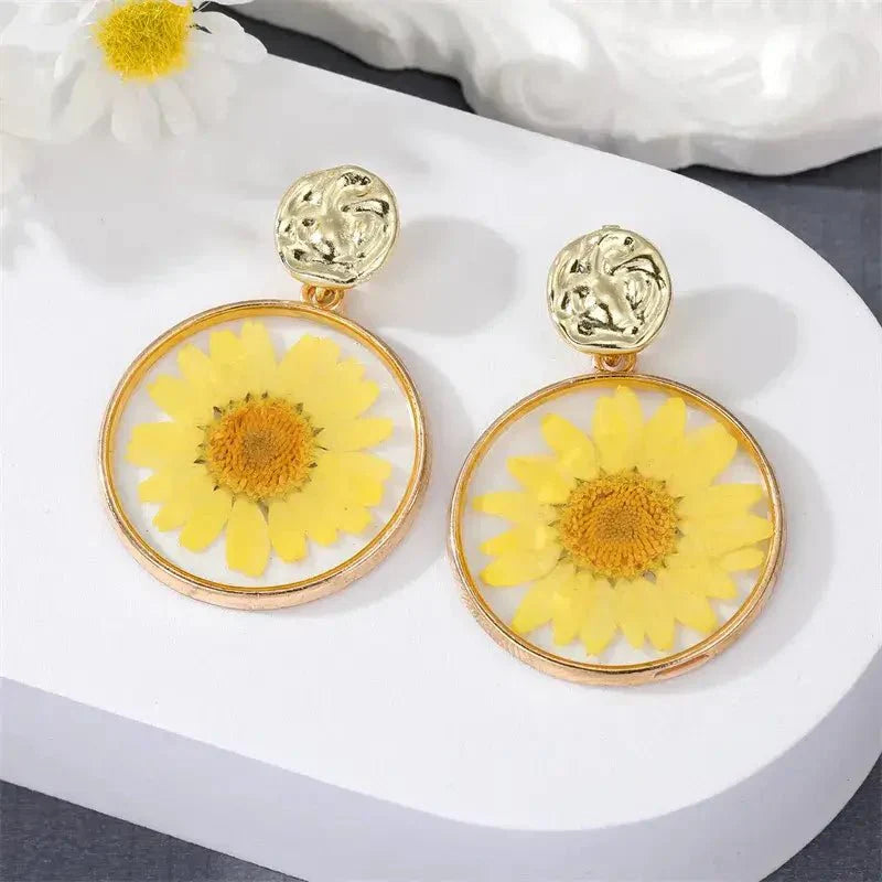 A close-up of a purple pressed flower boho earring with a gold-toned hammered stud.