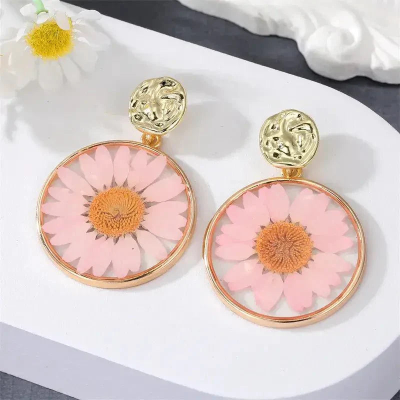 A close-up of a pink pressed flower boho earring with a gold-toned hammered stud.