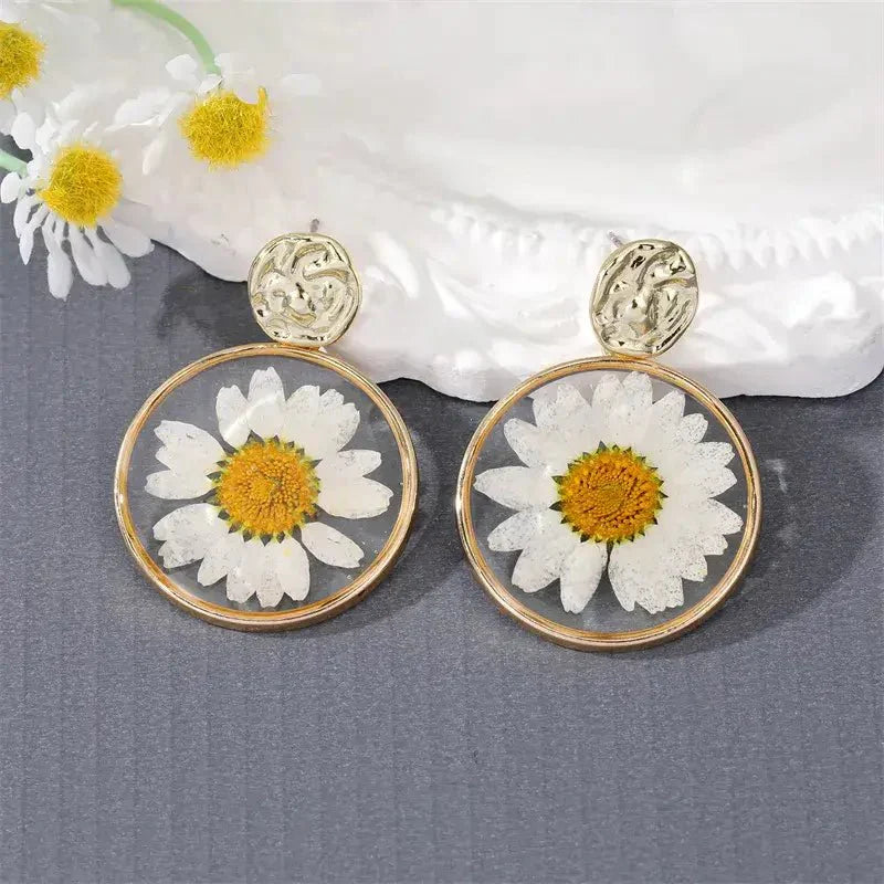 A close-up of a red pressed flower boho earring with a gold-toned hammered stud.