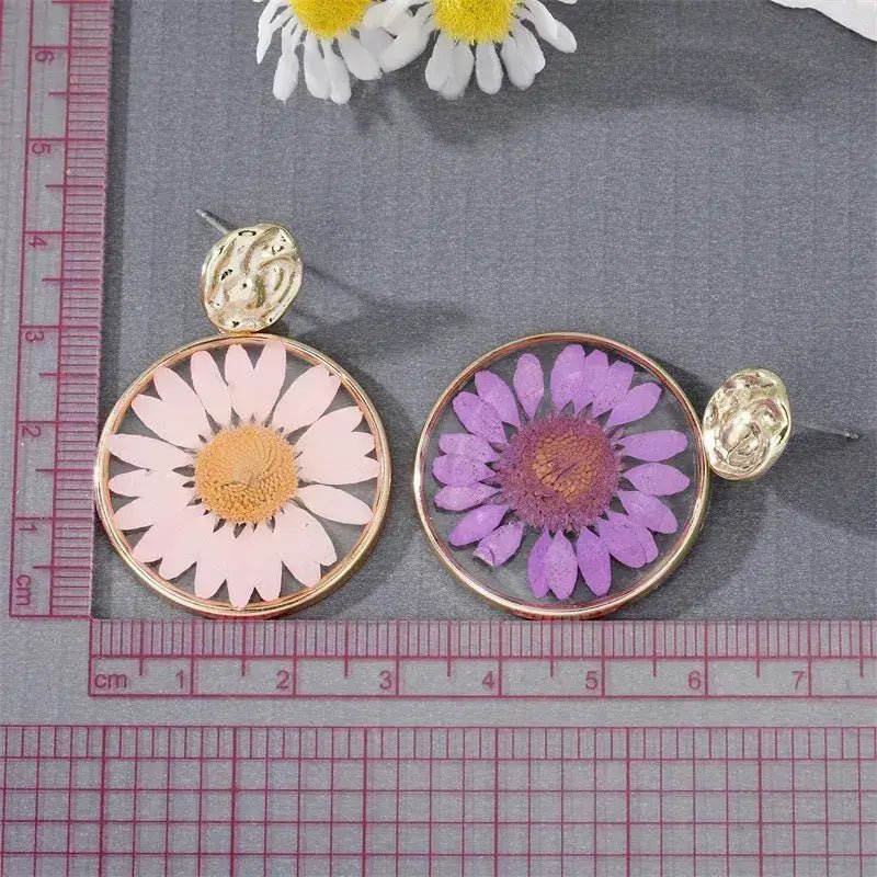 A close-up of a yellow pressed flower boho earring with a gold-toned hammered stud.