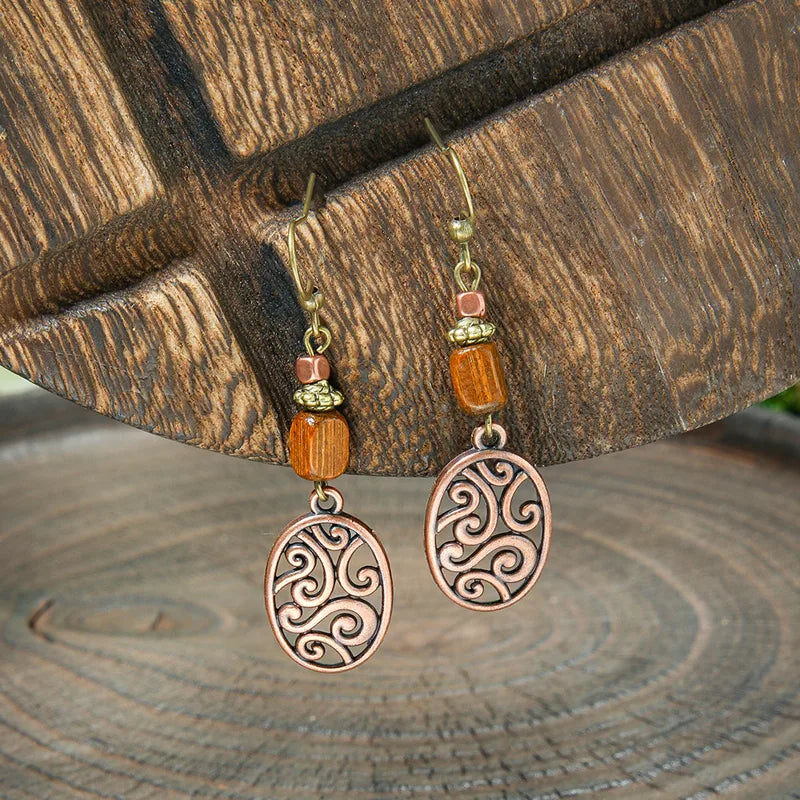Close-up of a pair of boho earrings featuring rustic wood beads and oxidised copper filigree dangles, hanging against a wooden background.