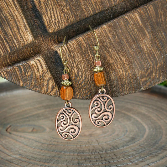 Close-up of a pair of boho earrings featuring rustic wood beads and oxidised copper filigree dangles, hanging against a wooden background.