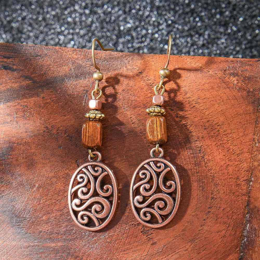 A pair of boho earrings with wood accents and oxidised filigree dangles, displayed against a rustic wooden surface.
