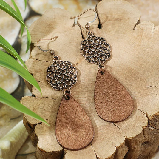 A pair of boho wooden earrings featuring bronze filigree tops and natural brown wooden teardrop drops, displayed on a wooden surface.