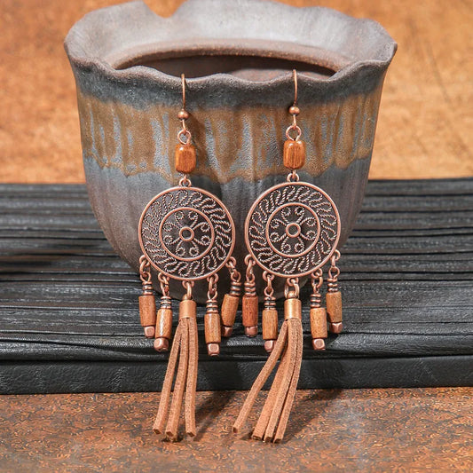 A pair of boho earrings with oxidised circular filigree design, wooden beads, and faux suede tassels, resting in a ceramic pot.