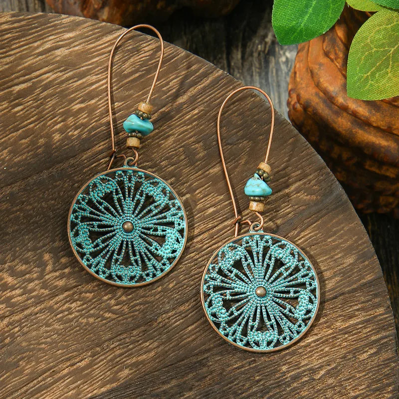 A pair of round oxidised earrings with intricate turquoise filigree patterns and small turquoise stone accents, displayed on a wooden surface.