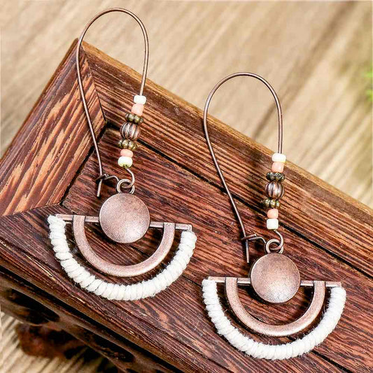 A pair of boho earrings with oxidised metal half-moon shapes wrapped in white thread, hanging from ear hooks with small beads, displayed on a wooden surface.