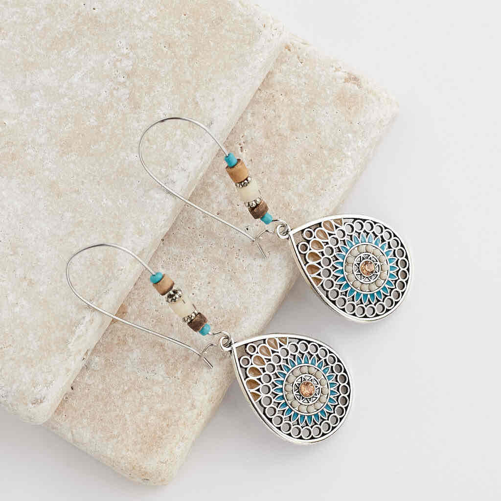 Two boho earrings featuring oxidised silver teardrop mandalas with turquoise and brown accents, laid on a light stone surface.