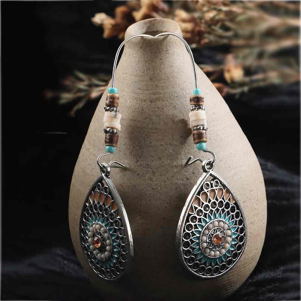 Two boho earrings featuring oxidised silver teardrop mandalas with turquoise and brown accents, laid on a light stone surface.