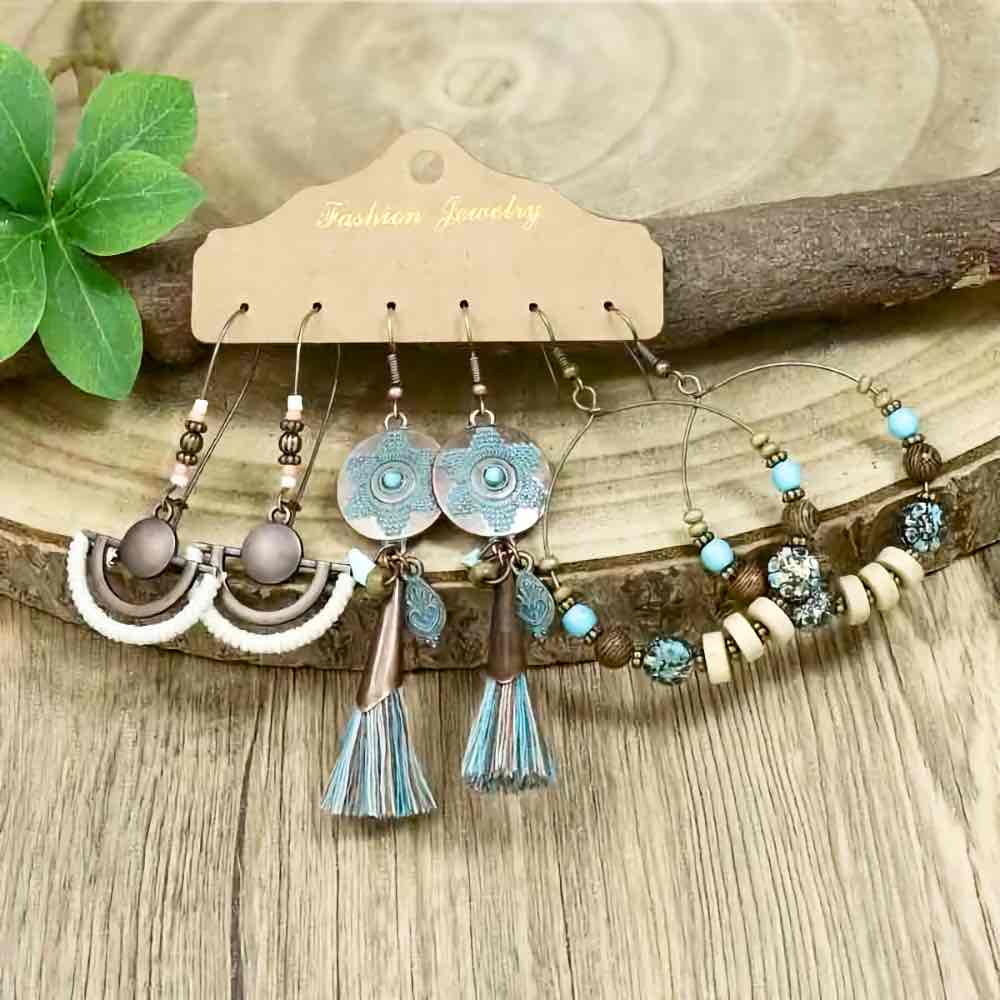 A set of three pairs of boho earrings displayed on a wooden surface, featuring oxidised metal, beads, and tassels.
