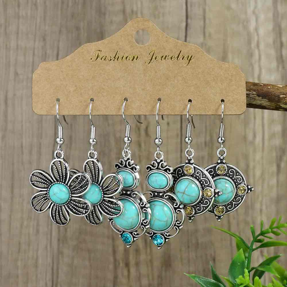 A set of three pairs of boho earrings with turquoise stones and silver-toned metal, displayed on a brown cardboard card.