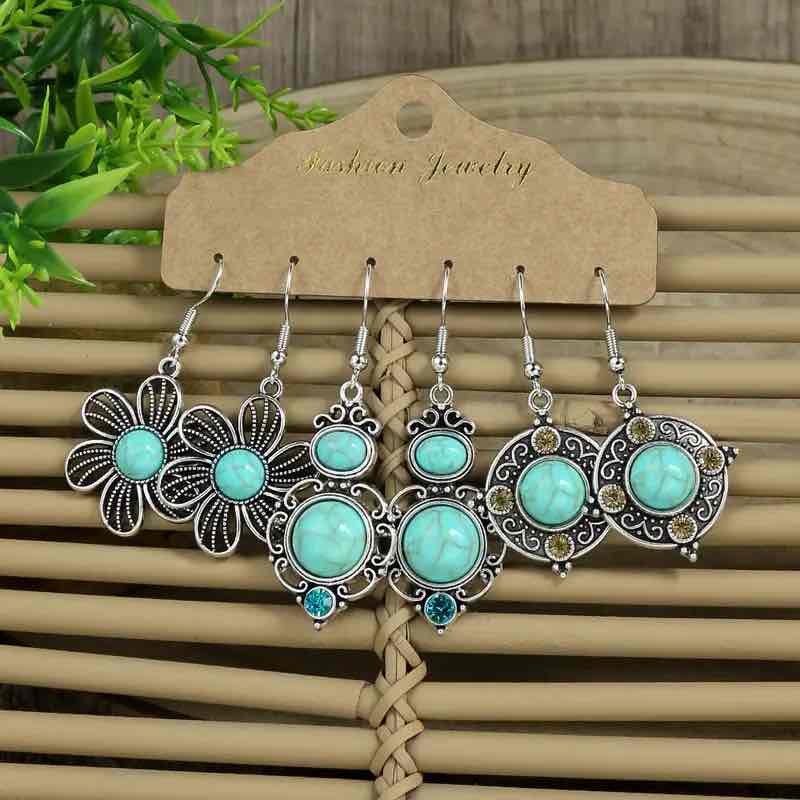 Three pairs of boho earrings, each featuring turquoise stones and intricate silver-toned designs, arranged on a woven mat.