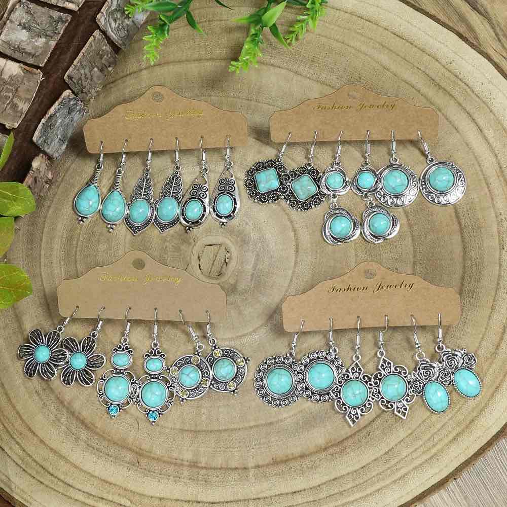 Four different sets of boho earrings, each with turquoise accents and silver-toned metal, displayed on a wooden surface with green foliage.
