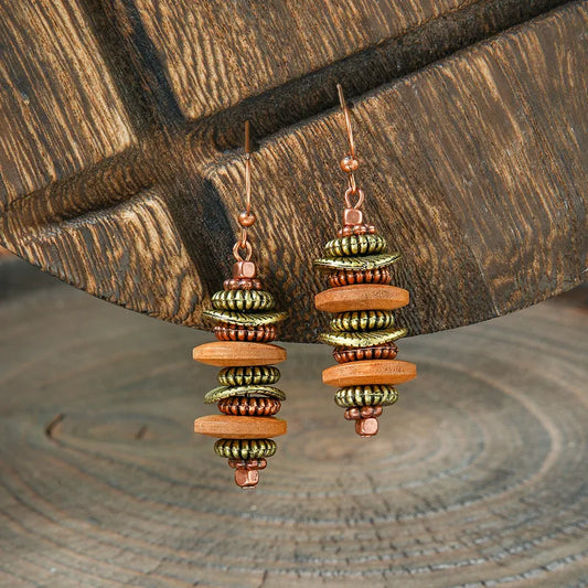 A pair of boho earrings with stacked wooden and metallic beads in brown, gold, and copper, hanging against a rustic wooden background.