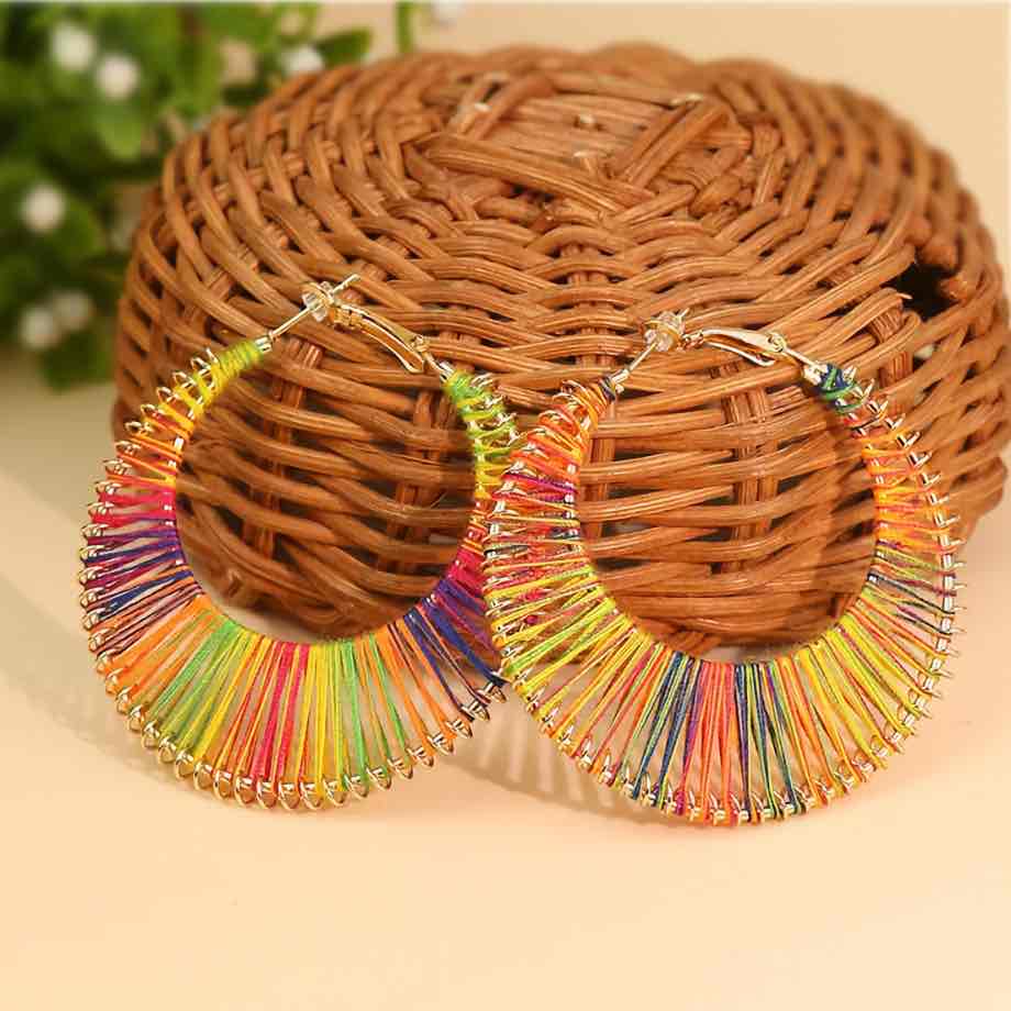 A pair of vibrant rainbow thread-wrapped boho earrings displayed against a woven basket.