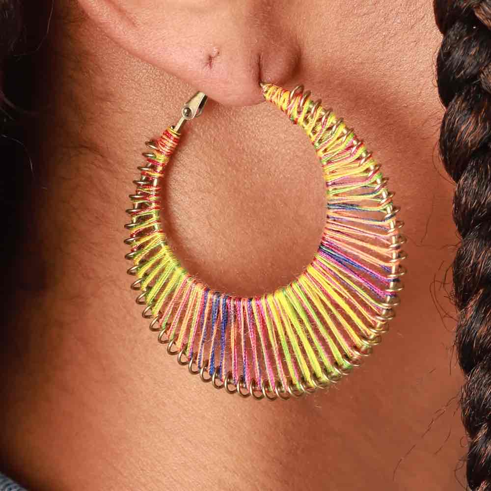 A close-up shot of a single rainbow thread-wrapped boho earring being worn on an ear.