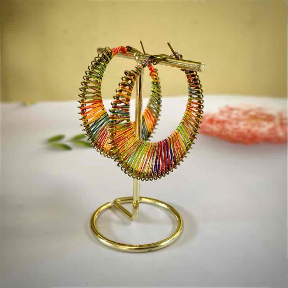 A pair of rainbow thread-wrapped boho earrings displayed on a gold earring stand.