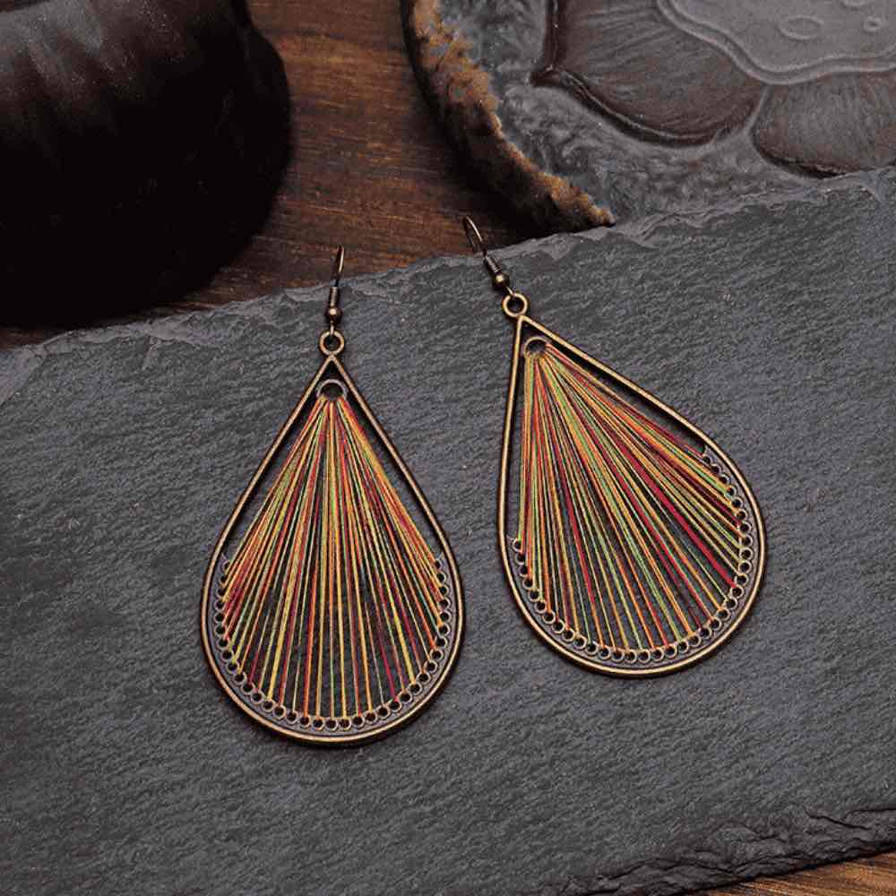 A pair of multicolor threaded boho earrings displayed on a dark slate surface, showcasing their intricate design.